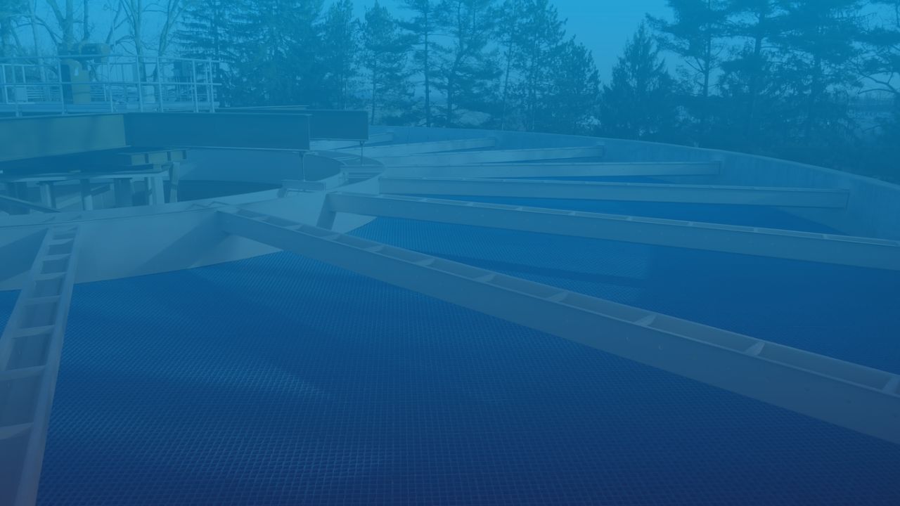 A large, circular tank, part of a water treatment plant. The image has a bluish tint.