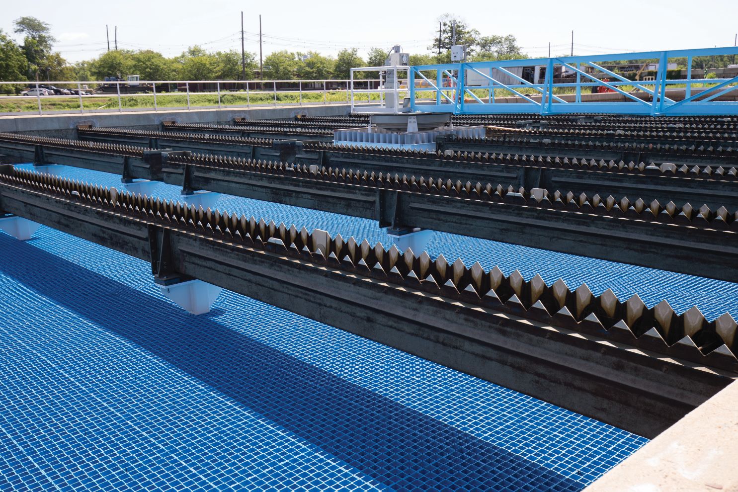 Imagen que muestra los tanques de sedimentación de una instalación de tratamiento de aguas. Los tanques tienen una serie de barreras inclinadas en forma de peine para ayudar a la sedimentación. El agua aparece limpia y clara, con un fondo de azulejos azules.