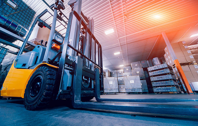 An image of a warehouse with a bright orange light. In the forefront is a yellow forklift.