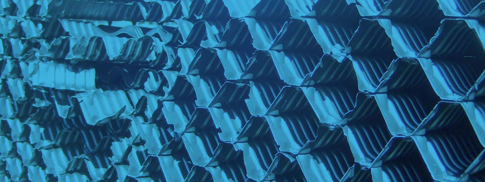 A close-up shot of multiple rows of stacked, blue, corrugated metal sheets. The sheets form a repetitive pattern with their V-shaped folds, creating a geometric and textured visual effect reminiscent of structured learning materials. The image has an overall cool blue tint.